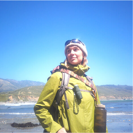 Hiker in a green rain jacket on a sunny coastline