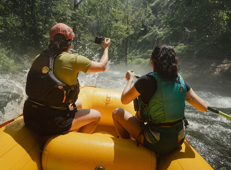 Two rafters in whitewater, one holding a camera up to the spray